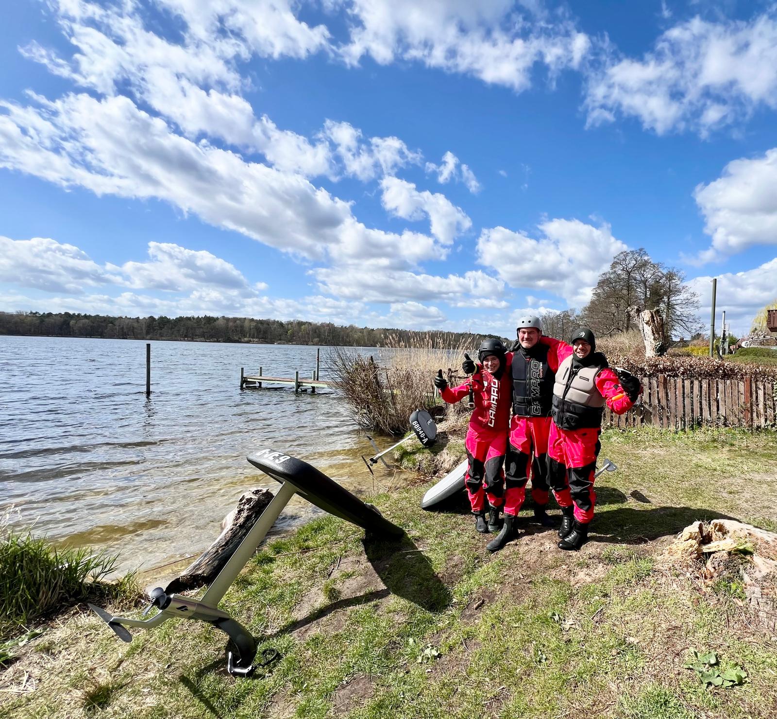 Drei begeisterte eFoil-Kursteilnehmer mit Daumen hoch nach ihrer Session am See